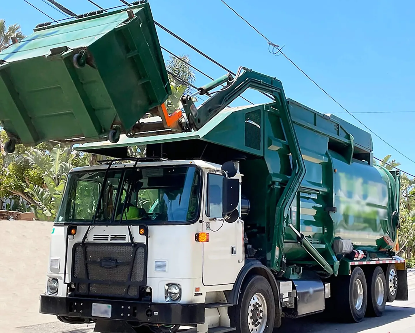 A commercial front end garbage truck lifting a four yard dumpster