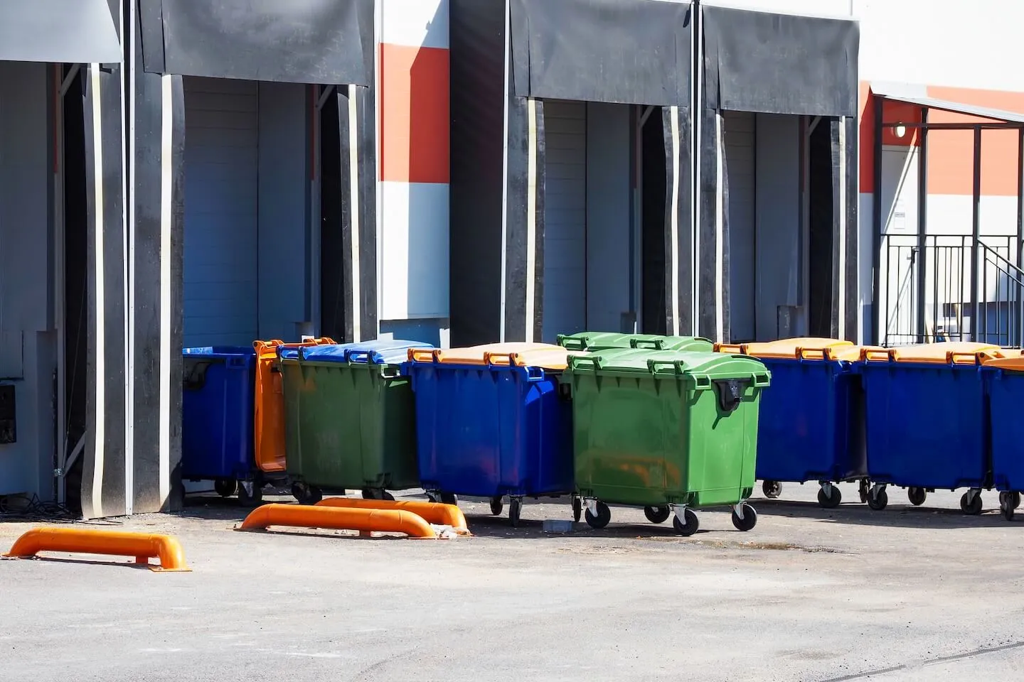 Blue and green dumpsters lined up in front of loading dock doors