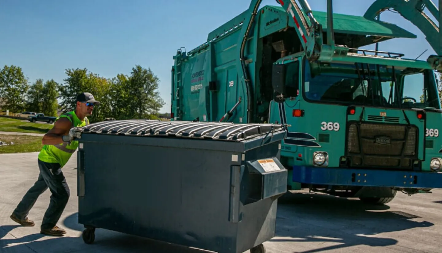 Man pushing front load dumpster in front of garbage truck