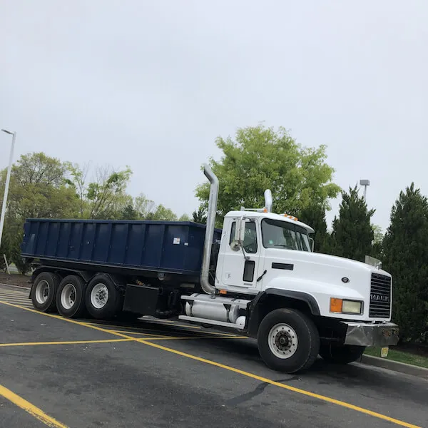 Dumpster truck in parking lot with trees behind it